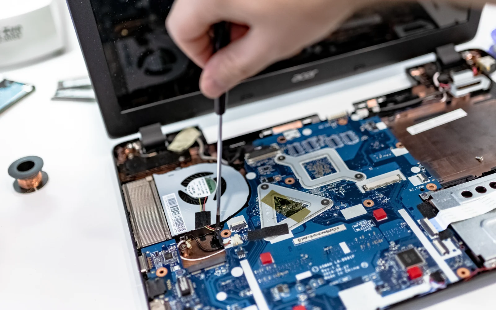 Hands working on a laptop motherboard with a screwdriver