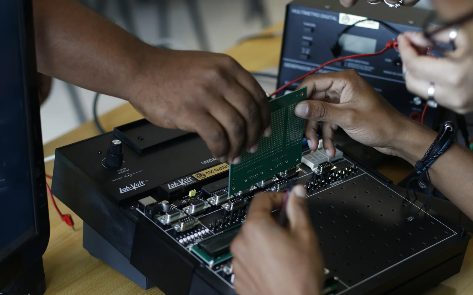 Hands connecting a circuit board on an electronics test bench